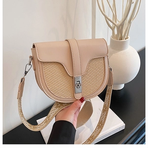 Detail of a beige saddle bag with woven straw panels and adjustable patterned strap