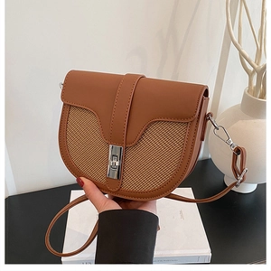 Detail of a brown leather saddle bag featuring a woven straw panel and silver turn-lock