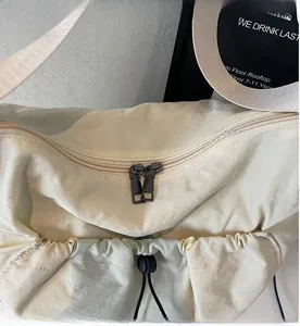 Detail view of dual metal zippers and adjustable drawstring on beige nylon hobo crossbody bag