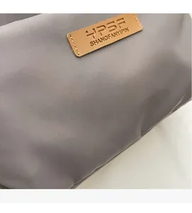 Close-up of grey nylon fabric texture and brown leather logo tag on the crossbody bag