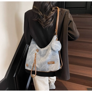 Detail of distressed blue hobo bag with brown leather strap and small round pendant