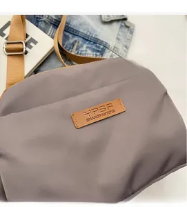 Close-up of gray nylon crossbody bag with leather brand logo and adjustable strap