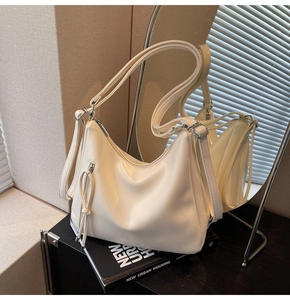 Close-up of cream PU leather shoulder bag with zipper pocket and long fringe tassels