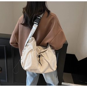 Detail of adjustable drawstring closure and wide woven strap on oversized cream crossbody bag