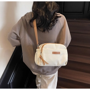 Rear view of a cream crossbody bag with brown leather accents and adjustable strap