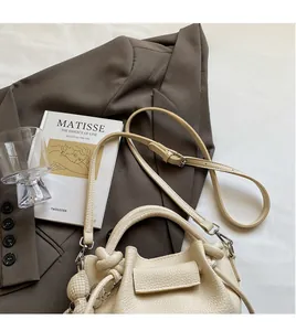 Detail of cream lychee texture leather bucket bag with long strap and side knot detail