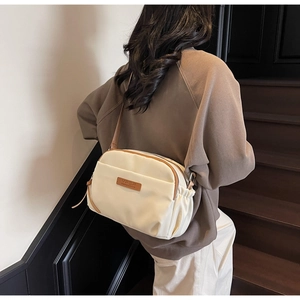 Detail of a cream nylon crossbody bag featuring a brown zipper and side pleated design