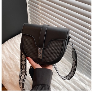 Detail of black saddle bag with woven texture, silver rotating lock and ethnic strap