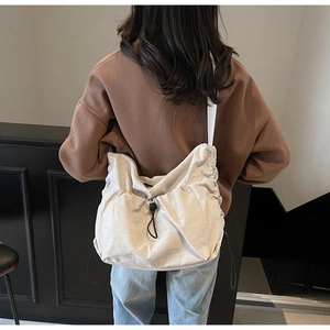 Model wearing a cream nylon drawstring crossbody bag with wide strap in a minimalist setting
