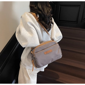 Detailed view of grey nylon crossbody bag with multi-zipper pockets and leather logo