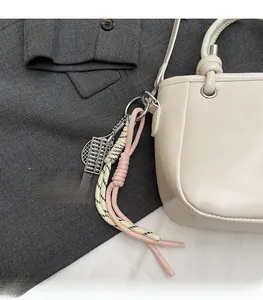 Detailansicht eines silbernen Abakus-Anhängers mit Kordeln an einer beigen Handtasche
