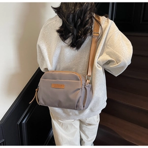 Detailed view of grey nylon crossbody bag with brown strap on a model on stairs