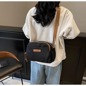 On-body shot of black nylon crossbody bag featuring double zippers and brown trim accents