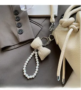 Detail of beaded pearl keychain with beige plaid bow on cream leather bucket bag