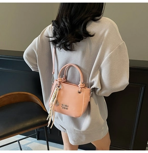 Sac seau rose avec pompons et bandoulière porté par un mannequin dans un cadre élégant