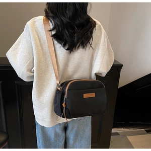 Detail of a casual black crossbody bag with brown strap and leather zipper tassels on a model