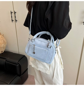 Dettaglio della borsa bowling azzurra con tasca con zip e pendente a cuore in metallo