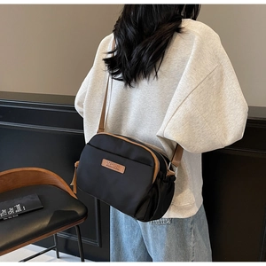 Rear view of black nylon crossbody bag with brown straps and multi-layer zipper design