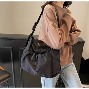 Detail of adjustable strap buckle and drawstring design on black nylon shoulder bag