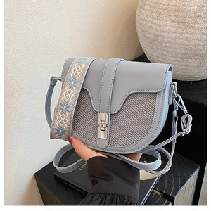 Detail of light blue saddle bag with textured fabric and floral embroidered wide strap