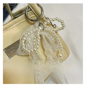 Detail view of a white lace bow and faux pearl bead bag charm with a silver spring clasp