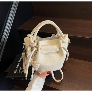Close-up of cream pleated bucket bag featuring litchi texture and elegant pearl bow pendant