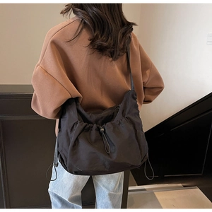 Detail of black pleated nylon hobo bag with drawstring closure on model's shoulder