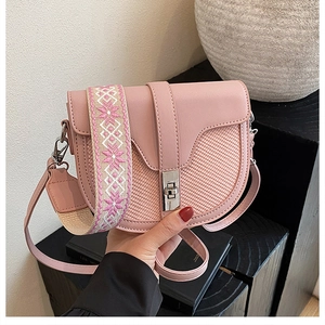 Detail of pink saddle bag with woven texture, metal clasp, and floral embroidery strap