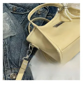 Detail view of beige bow shoulder bag with pearl pendant and metal plaque detail