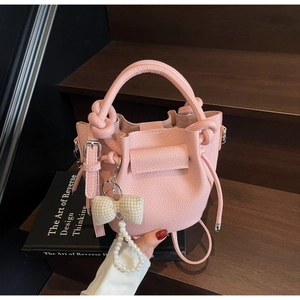 Pink lychee grain leather bucket bag featuring white pearl charms and a bow detail