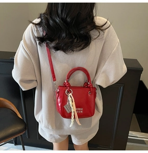 Détail du sac seau en cuir rouge avec lettrage en métal argenté et breloque tressée