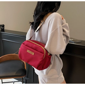Detailed view of burgundy nylon crossbody bag with multi-zipper compartments and wide strap