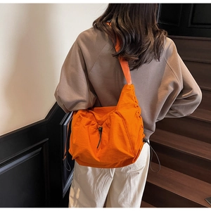 Detail of bright orange nylon crossbody bag with side drawstring and wide strap