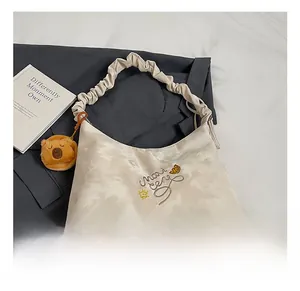 Dettaglio di una borsa tote crema con ricamo giallo e ciondolo a forma di orso