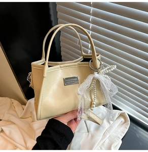 Detailed close-up of cream PU leather handbag with elegant pearl lace bow accessory
