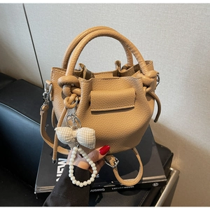 Detail of khaki lychee leather bucket bag with pearl charm and bow hanging on the side