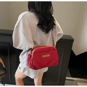 Detailed view of red nylon crossbody bag with multiple zippers and brand logo patch
