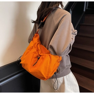 Detail of vibrant orange nylon crossbody bag with decorative drawstrings and buckles