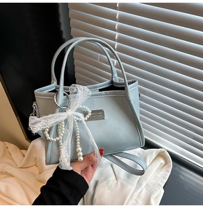 Detail of light blue trapezoid handbag with pearl charm and white lace bow decoration