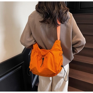Detail of a bright orange crossbody bag with adjustable drawstring and wide strap
