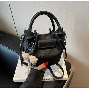 Detail of black lychee grain leather bucket bag with pearl bow charm and top handles