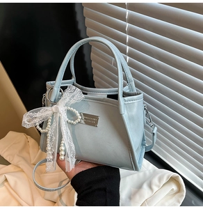 Detail of light blue faux leather bag with lace bow and elegant pearl strap