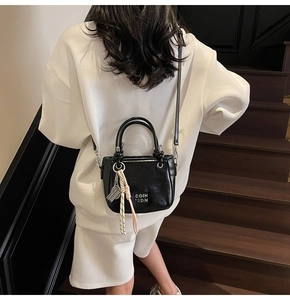 Détail d'un sac seau noir brillant avec lettres métalliques et breloque en cordon tissé