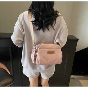 Detailed back view of a pink nylon crossbody bag with wide strap on a female model