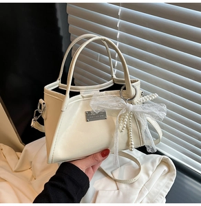 Close-up of cream bow shoulder bag with pearls and silver brand plate detail
