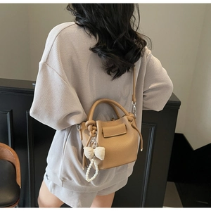 Detail view of khaki bucket bag with lychee texture and pearl bow charm accessory