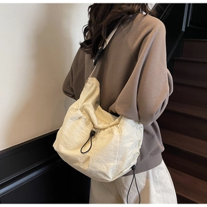 Detail of creamy white ruched shoulder bag showing drawstring closure and buckle strap