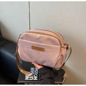 Detailed view of pale pink nylon crossbody bag with three zipper layers and brand logo