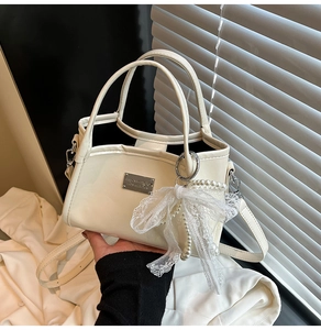 Detail of elegant bow and pearl charms on an ivory faux leather shoulder bag