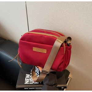 Close-up of a burgundy multi-zipper nylon crossbody bag with three storage compartments